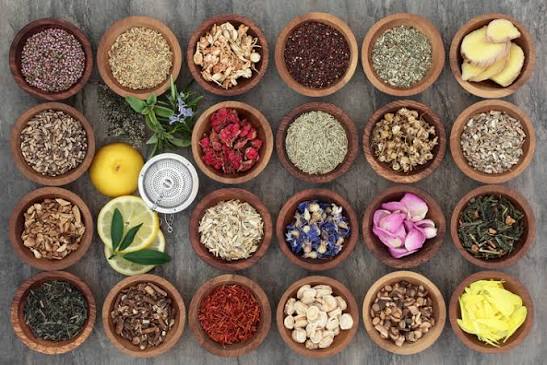 Wooden bowls filled with dried herbs, flowers, roots, and citrus for herbal medicine making.